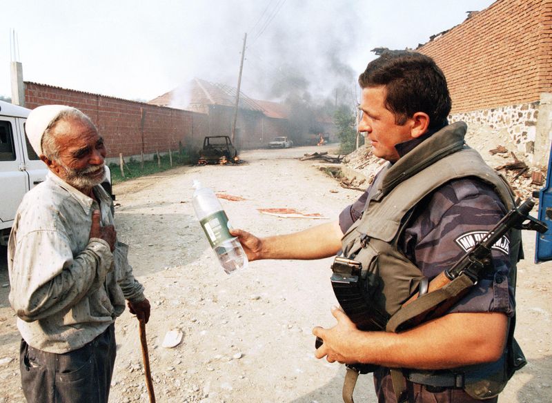 A Serbian Policeman offers water to an elderly ethnic Albanian villager, Kosovo